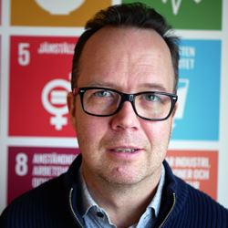 Porträtt av Jonas Frykman framför Agenda 2030 affisch Jonas Frykman